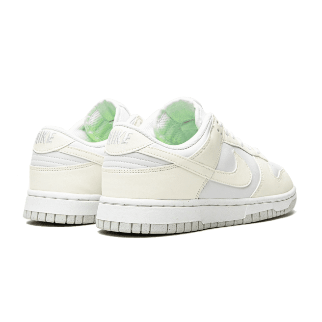 Vintage-stijl Nike Dunk Low Next Nature Sail sneakers met een off-white kleur en groen accent op een groene achtergrond.