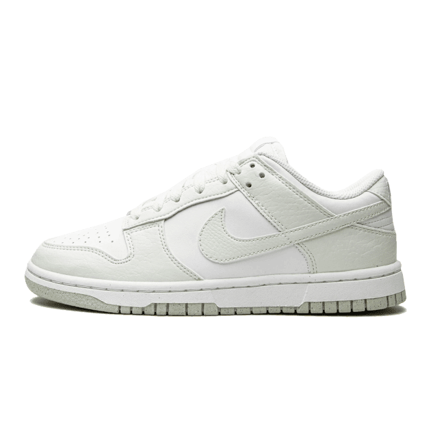 Witte Nike Dunk Low Next Nature sneakers met mint-accenten op een groene achtergrond