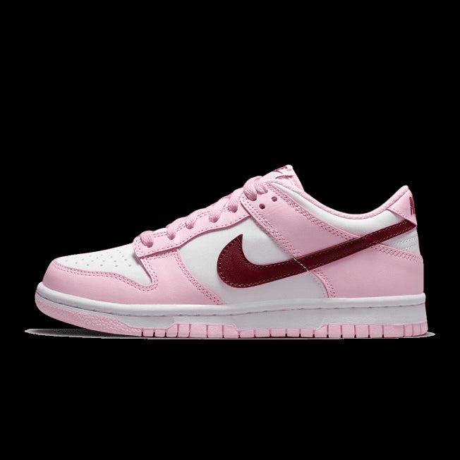 Roze en witte Nike Dunk Low sneakers met rode accenten. De sneakers hebben een klassiek silhouet en kenmerken van het Nike merk, zoals het Swoosh logo. De sneakers staan centraal op de foto tegen een effen groene achtergrond.