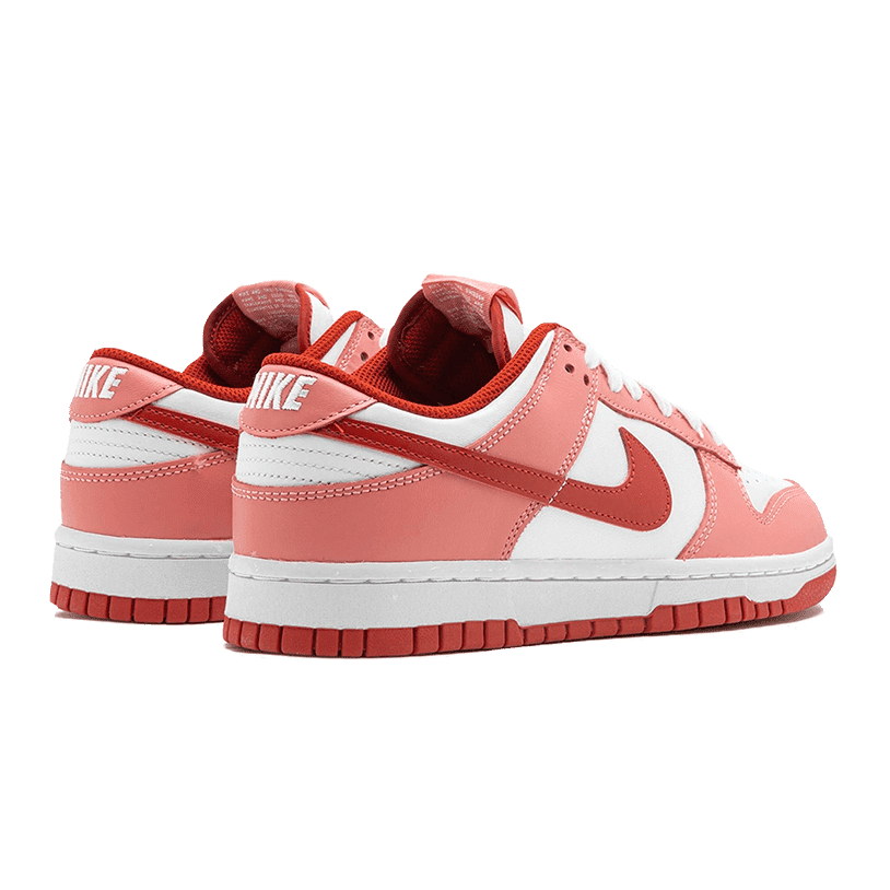 Roze en witte Nike Dunk Low sneakers met rode accenten op een groene achtergrond. Deze klassieke sneakers hebben een leren bovenwerk en een vintage stijl.