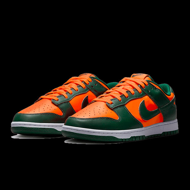 Oranje en groene Nike Dunk Low Retro Miami Hurricanes sneakers op een groene achtergrond. De schoenen hebben een felle oranje kleur gecombineerd met donkergroene accenten, wat een opvallend en stijlvol uiterlijk creëert. Dit model is geïnspireerd door de kleuren van de Miami Hurricanes en biedt een sportieve en trendy uitstraling.
