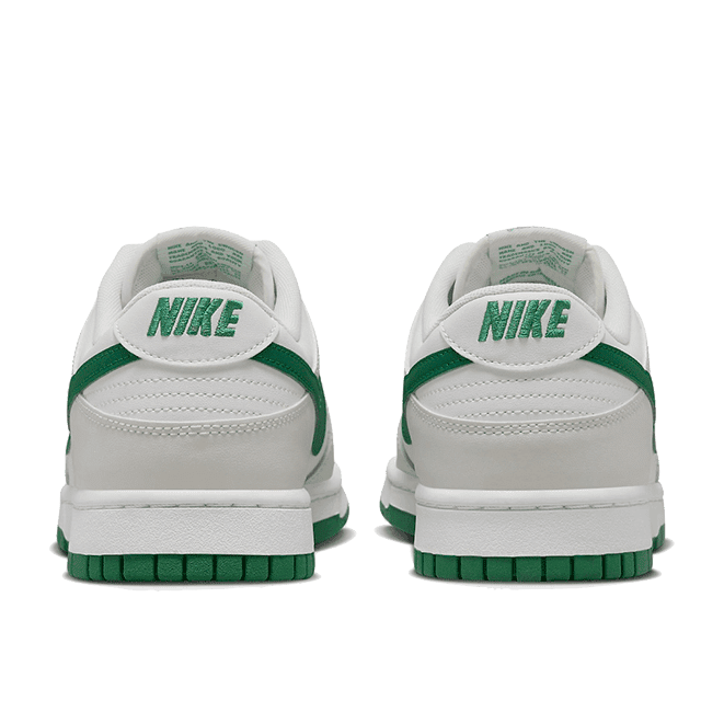 Witte Nike Dunk Low Retro Summit sneakers met malachietgroene accenten op neutrale groene achtergrond. De sneakers hebben een eenvoudig ontwerp met zichtbare Nike-branding op de zijkanten.