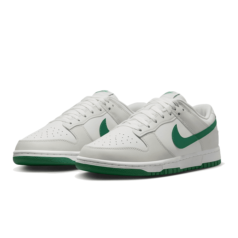 Witte Nike Dunk Low Retro sneakers met groene details op een groene achtergrond.