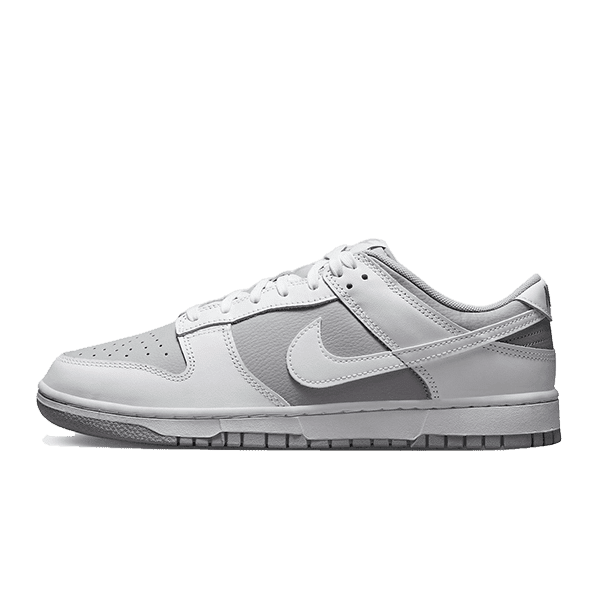 Klassieke Nike Dunk Low Retro sneakers in wit en grijs op een groene achtergrond.