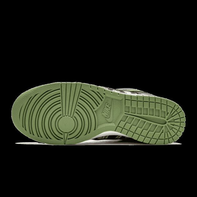Retro sneakers Nike Dunk Low SE met multicam-camouflagepatroon op een groene ondergrond.