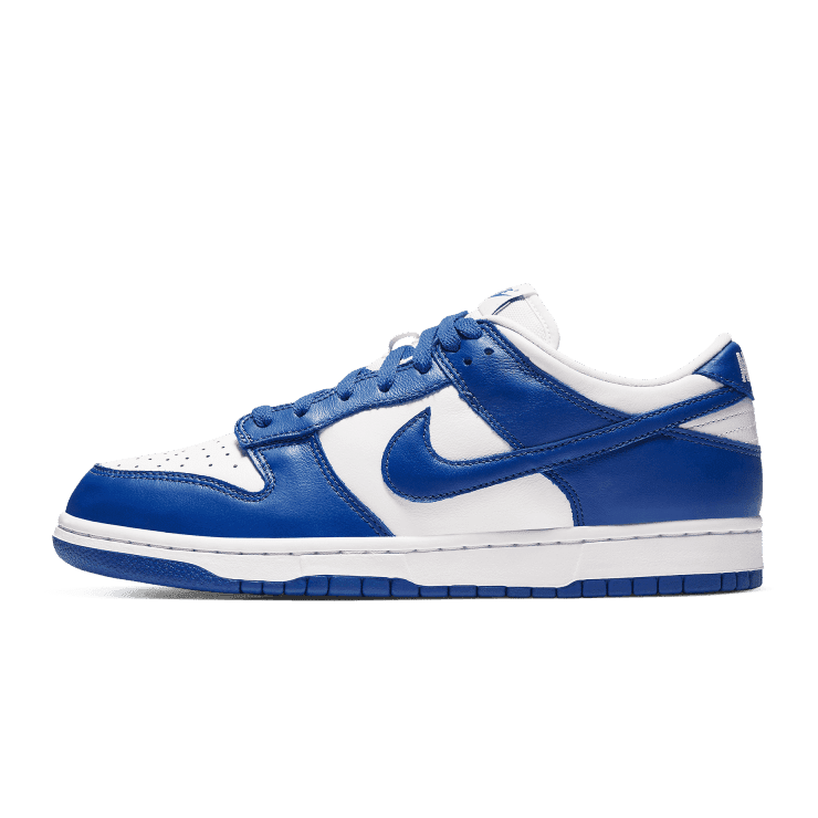 Blauwe en witte Nike Dunk Low SP Varsity Royal (Kentucky) sneakers tegen een groene achtergrond
