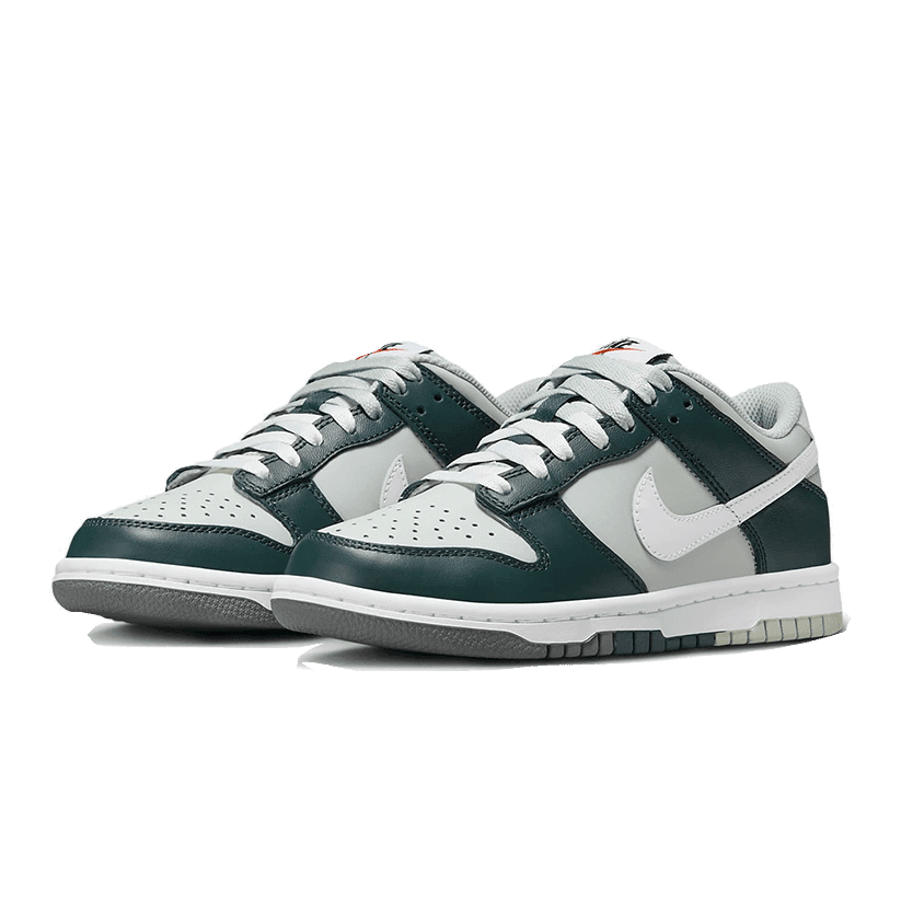 Grijze Nike Dunk Low Split Deep Jungle sneakers op een groene achtergrond. Deze sneakers hebben een wit en donkerblauw kleurenschema en lopen stijlvol af in een grijze zool.