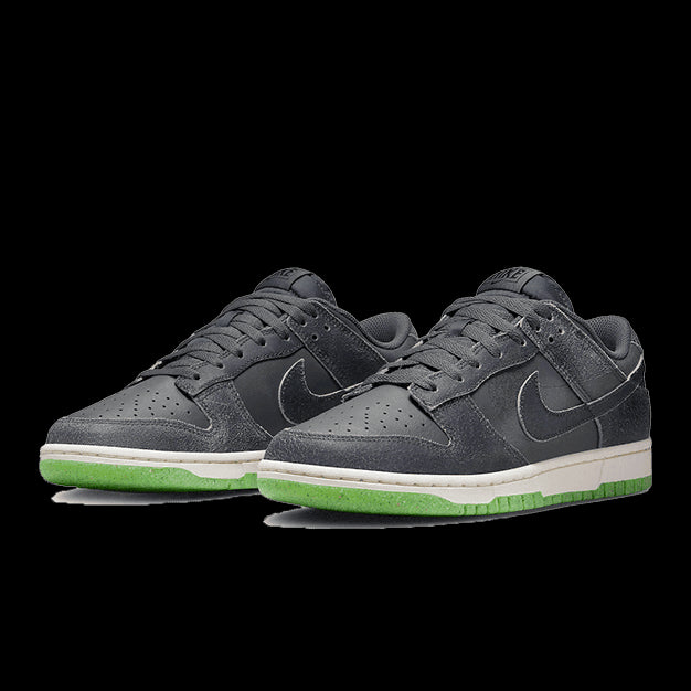 Donkergrijze Nike Dunk Low Swoosh Shadow sneakers op een groene achtergrond. De sneakers hebben een leren bovenwerk en een witte loopzool met een groene accentkleur.