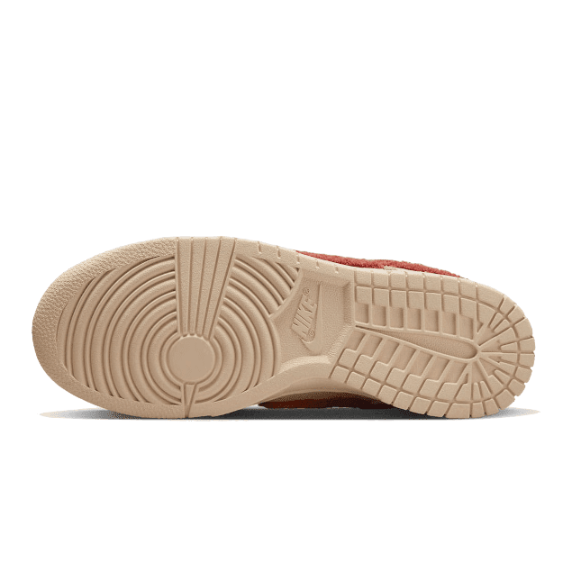 Exclusieve Nike Dunk Low Terry Swoosh sneakers tegen een groene achtergrond. De schoenen hebben een beige/terracotta kleurige zool met een golvend patroon en de iconische Nike Swoosh symbool is bedekt met een zacht Terry materiaal.
