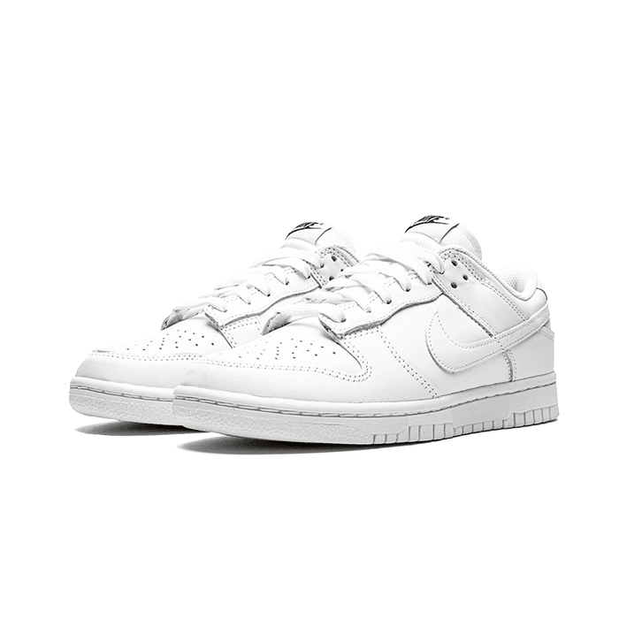 Elegante Nike Dunk Low Triple White (2021) sneakers op groene achtergrond. Deze stijlvolle, volledig witte sneakers met een sportief en minimalistisch design zijn een moderne klassieker.
