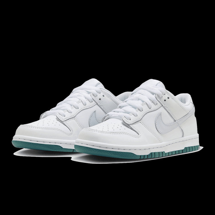 Witte Nike Dunk Low sneakers met grijze en tealblauwe accenten, op een groene achtergrond geplaatst.