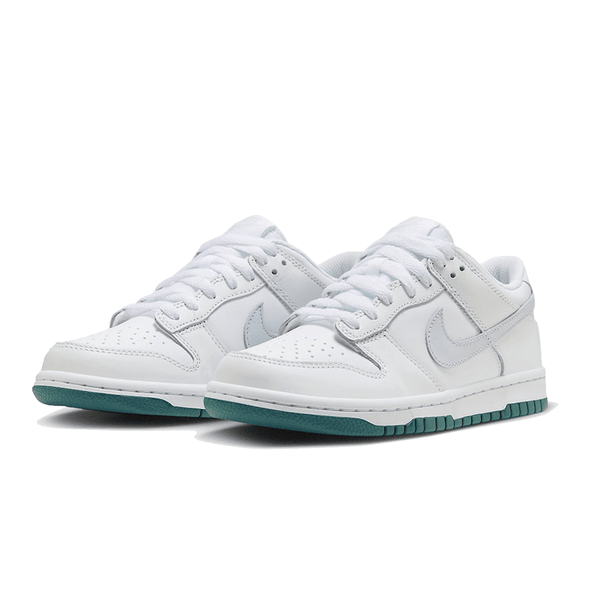Witte Nike Dunk Low sneakers met grijze en tealblauwe accenten, op een groene achtergrond geplaatst.
