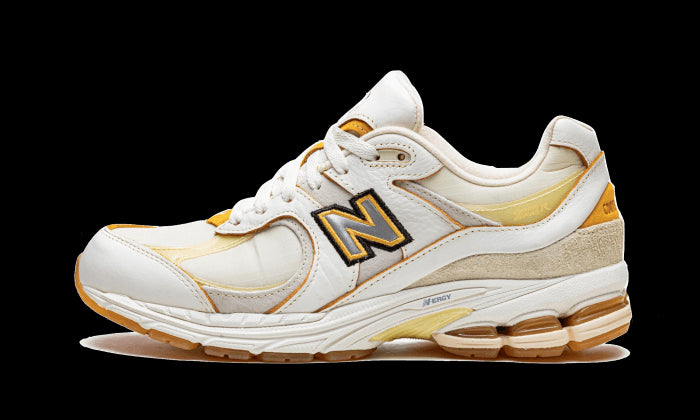 Nieuwe Balance 2002R sneakers in wit en goud, met het karakteristieke New Balance-logo. Deze sneakers laten een sportieve en stijlvolle uitstraling zien.
